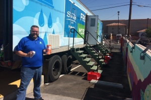 Man in a blue shirt standing beside a 'Clean the World: Fresh Start Mobile Showers' truck