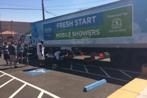 A group of people standing beside a 'Clean the World: Fresh Start Mobile Showers' truck