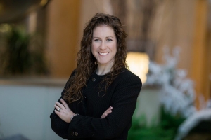 Jaime Miranda smiling in a black suit with her arms crossed