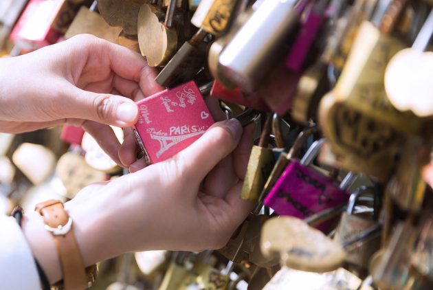 Hands latching a lock to a fence full of other locks